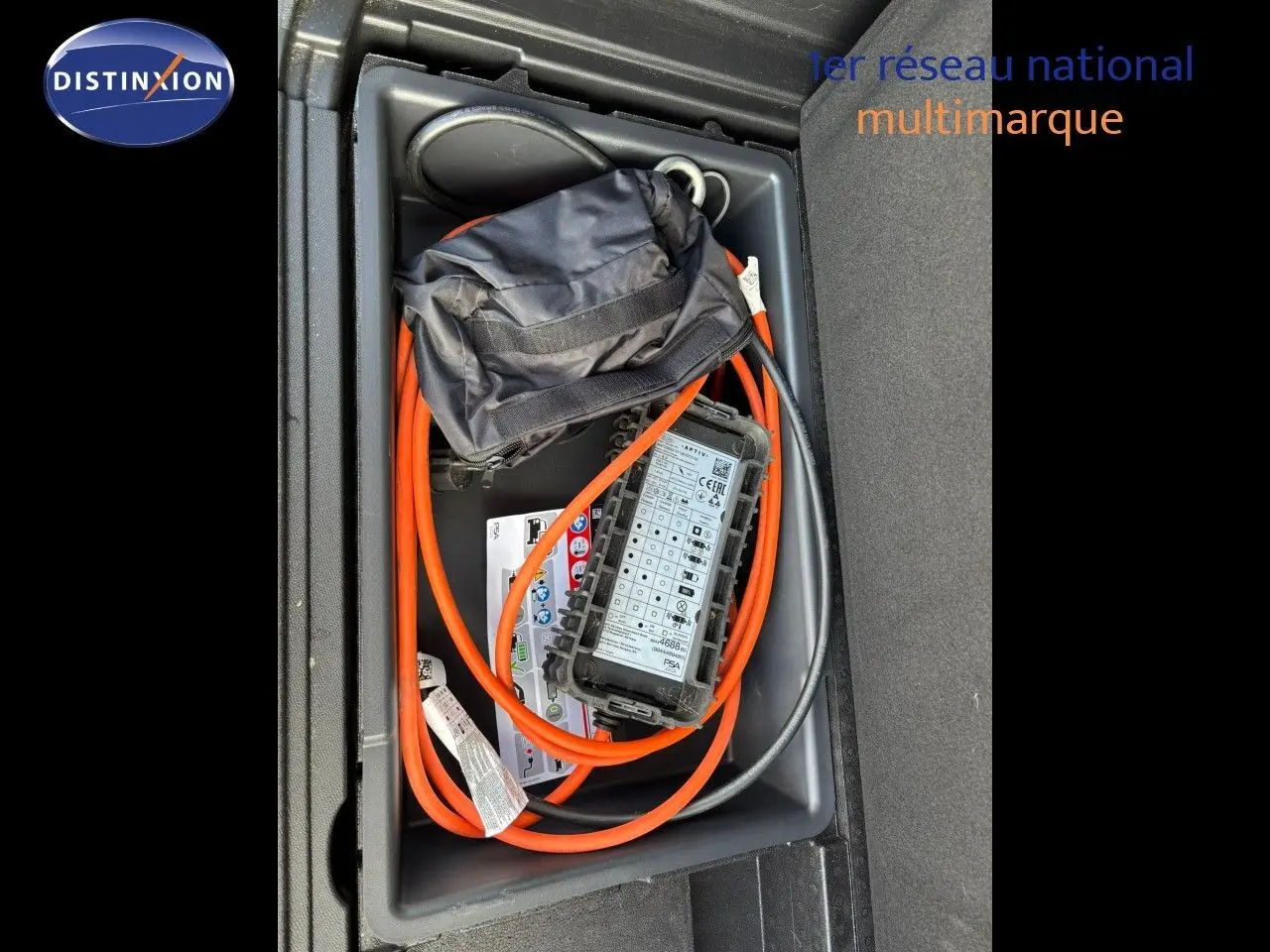 Coffre ouvert montrant le câble de recharge orange du Peugeot 3008 hybride gris platinium, vue plongeante sur le rangement.