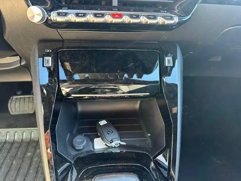 Gros plan sur la console centrale noire brillante du Peugeot 2008 1.2 Hybrid avec clé posée près de la prise 12V.