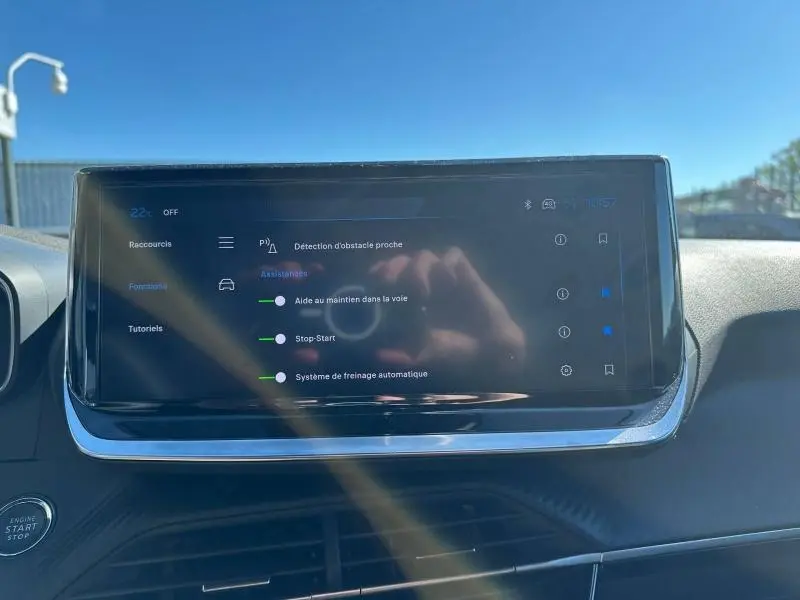 Écran tactile central du tableau de bord du Peugeot 2008 2025 affichant les aides à la conduite, avec reflet de mains.