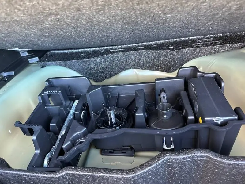 Vue rapprochée du rangement à outils sous le plancher du coffre d’un Peugeot 2008 bleu 2025 hybride.