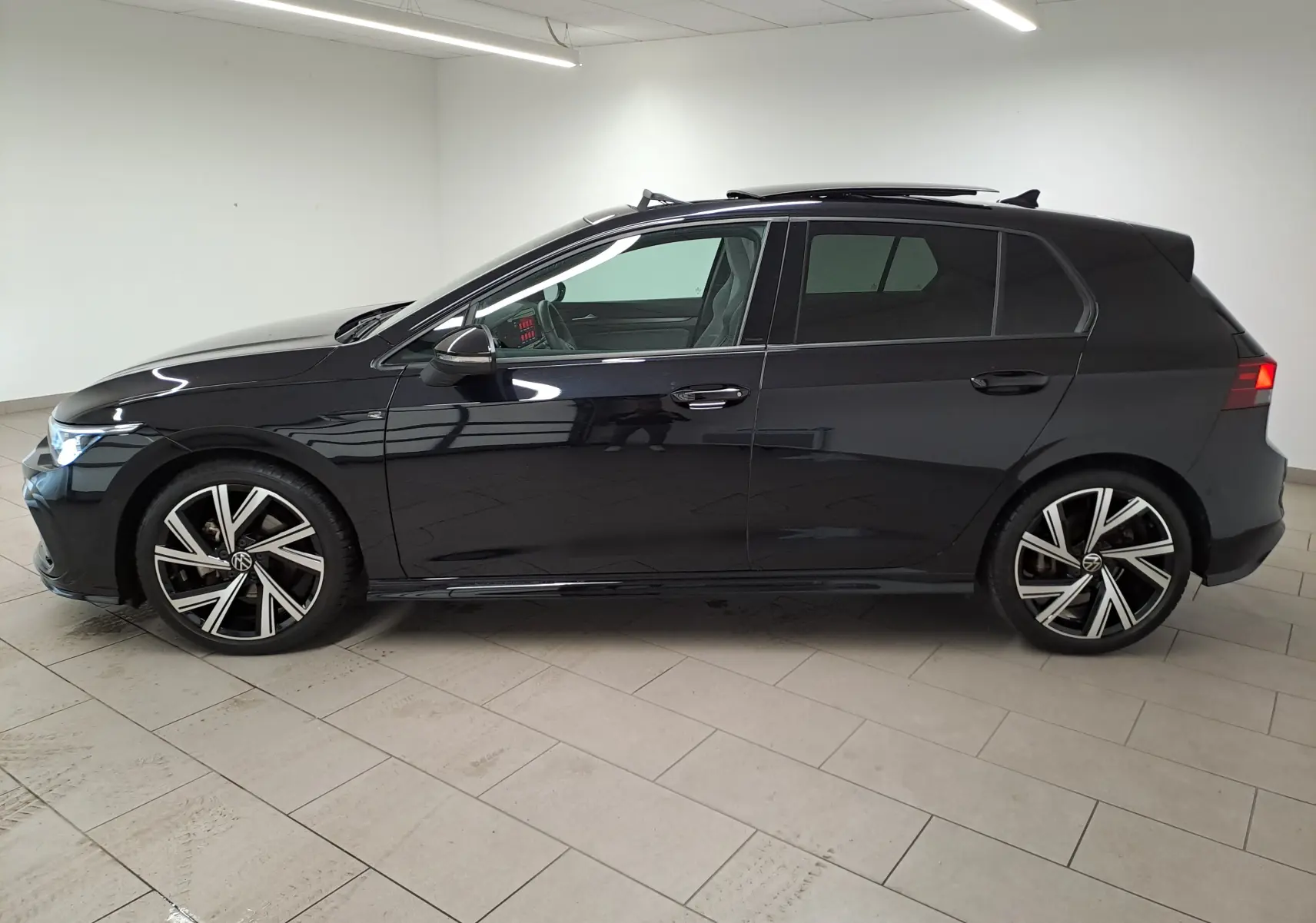 Profil côté gauche d'une Volkswagen Golf noire intense nacrée 2023 avec jantes alliage R-Line et toit ouvrant électrique.
