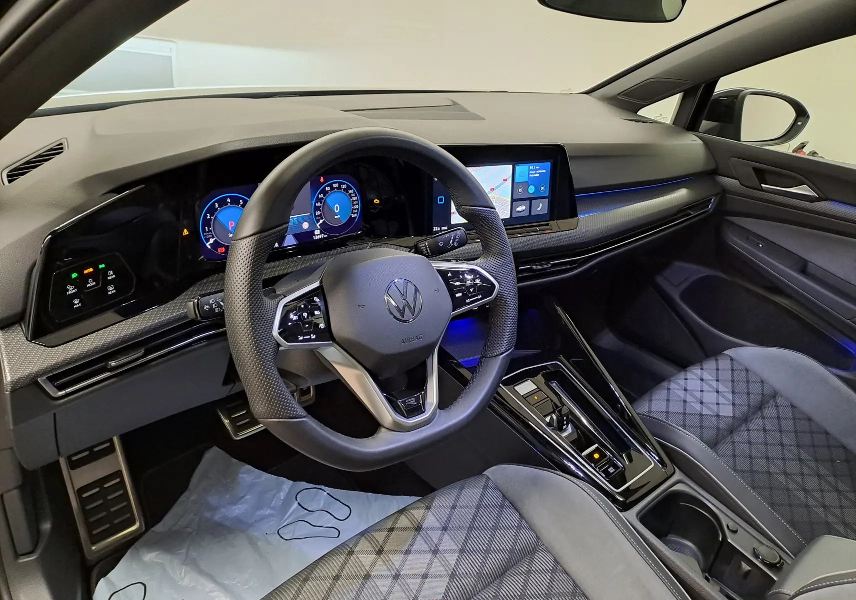 Vue intérieure avant droite de la Volkswagen Golf 1.5 eTSI 2023, volant cuir, tableau de bord digital et sièges tissu à motifs.