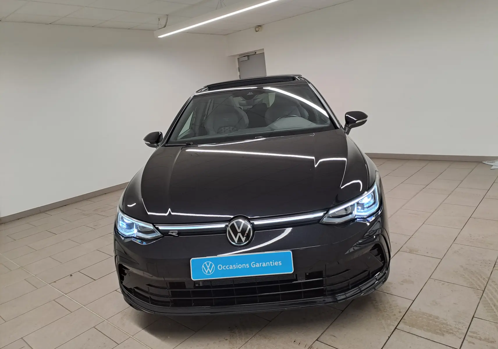 Vue avant frontale d'une Volkswagen Golf 1.5 eTSI R Line noire intense nacrée avec phares LED allumés et toit ouvrant visible.
