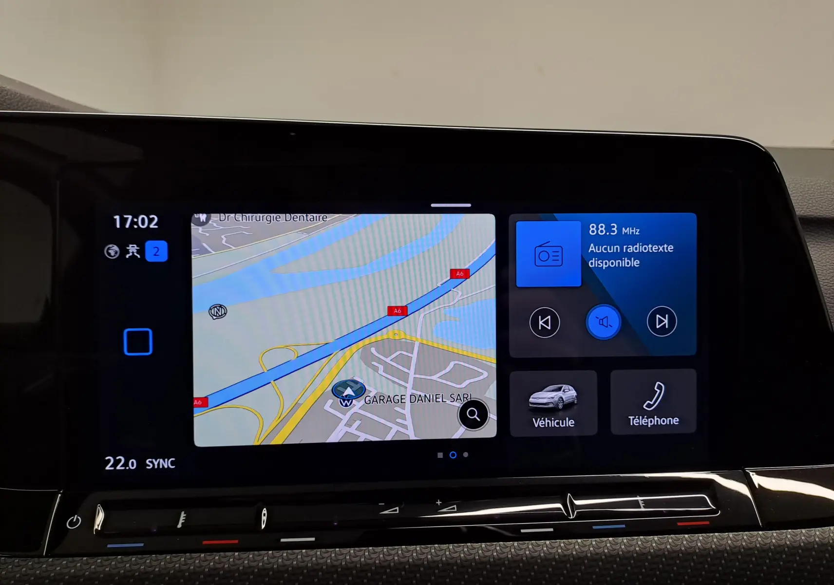 Écran tactile intérieur de la Volkswagen Golf 1.5 eTSI 2023 affichant la navigation et la radio, avec commandes climatisation en dessous.
