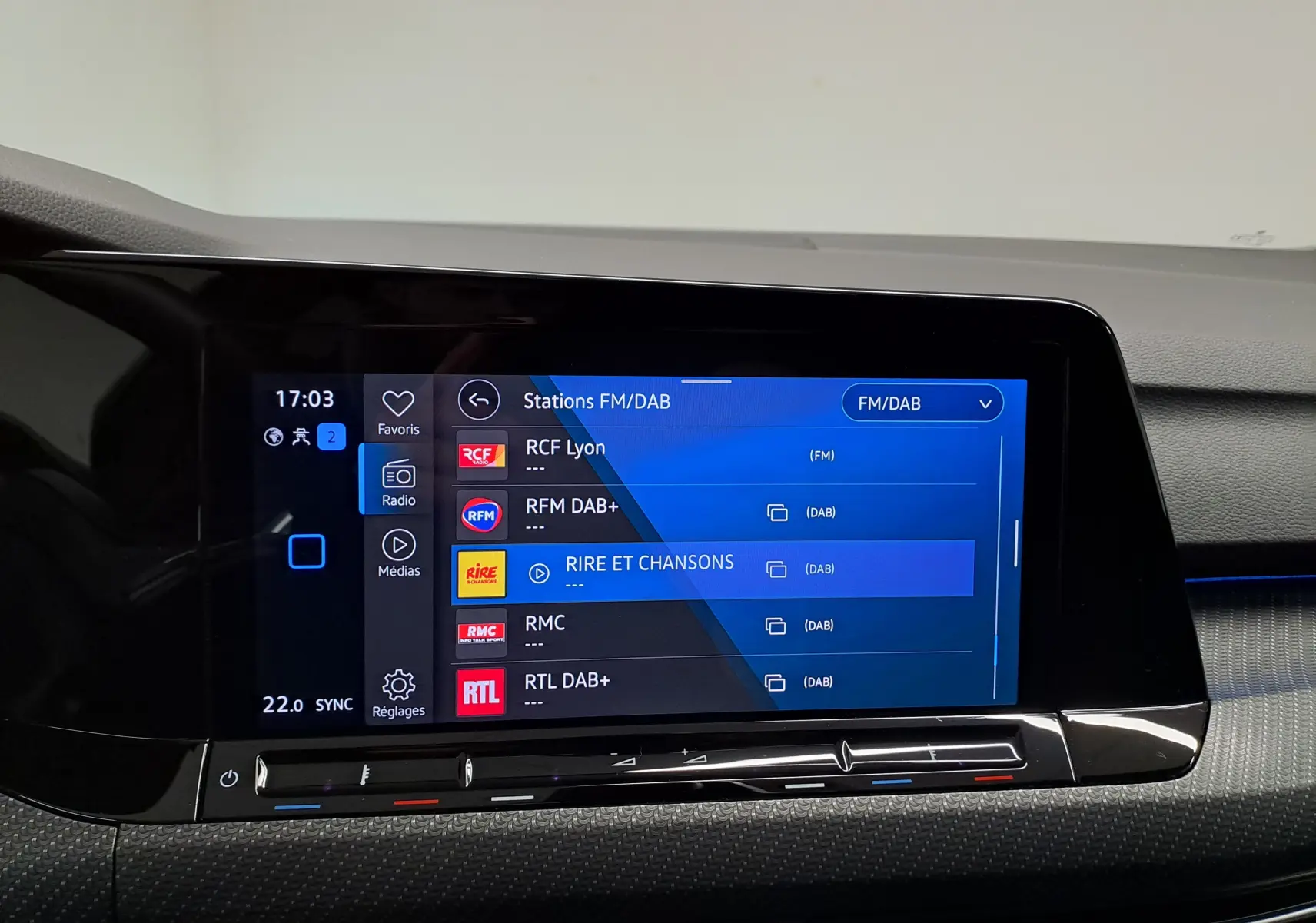 Écran tactile central de la Volkswagen Golf 2023 affichant les stations FM/DAB, avec tableau de bord noir.