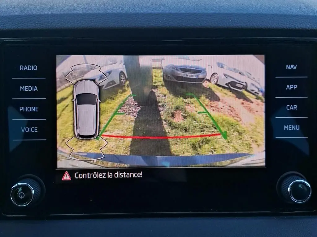 Écran de caméra de recul montrant l'arrière d'une Skoda Karoq bleu avec lignes de guidage vertes et rouges.