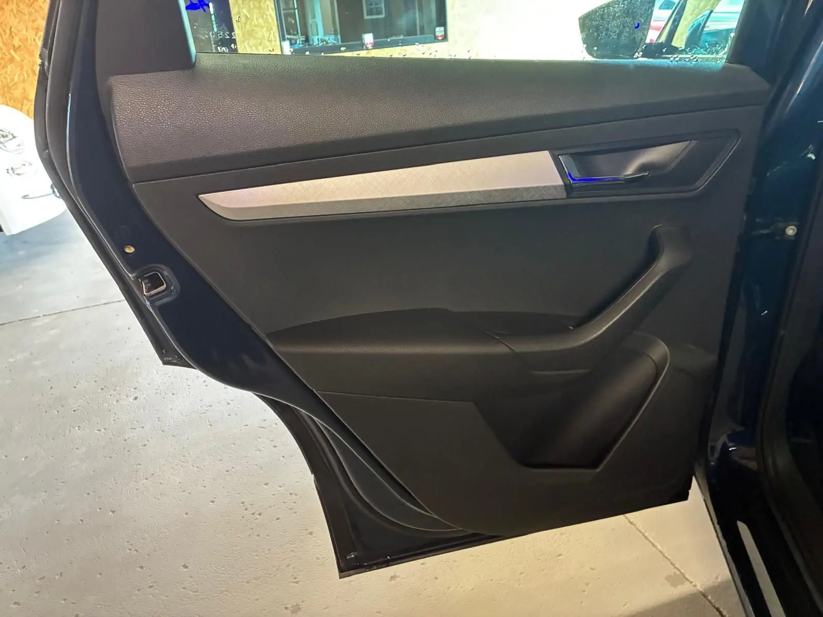 Vue rapprochée de la porte arrière gauche noire du Skoda Karoq bleu 2023 avec poignée intégrée et insert décoratif gris.