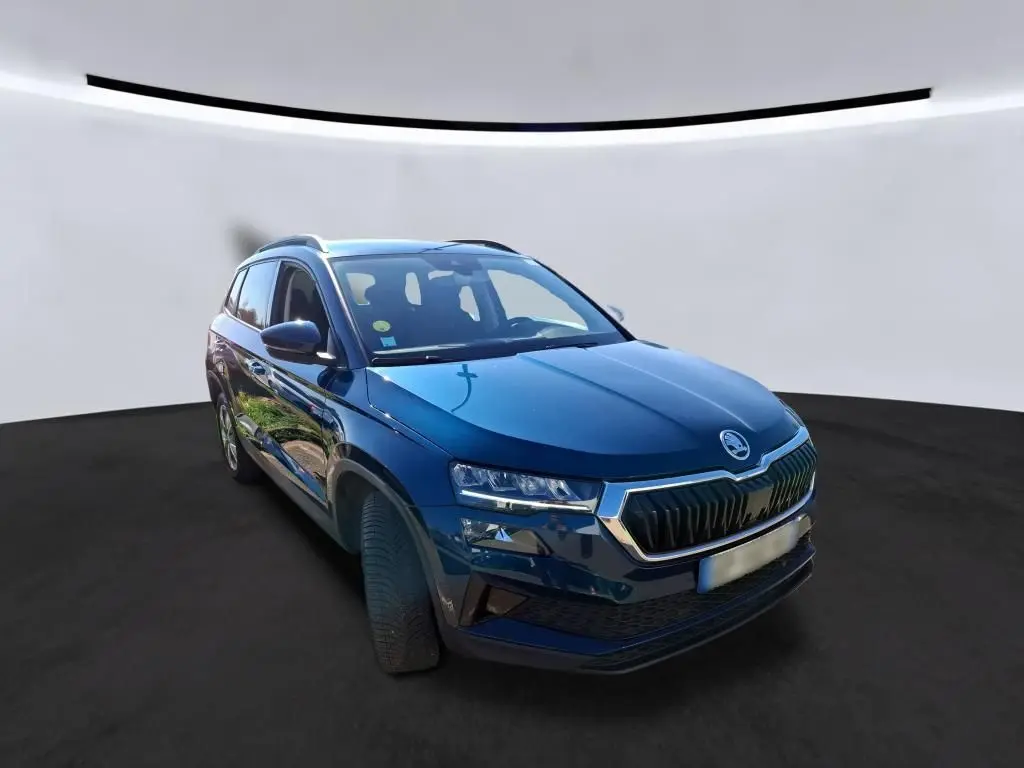 Vue 3/4 avant gauche d'un Skoda Karoq bleu métallisé avec calandre chromée et jantes alu 17 pouces sur fond neutre.
