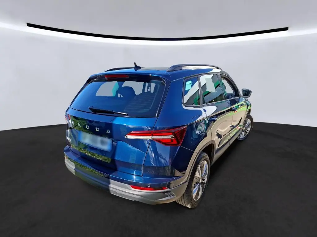 Vue 3/4 arrière droite d'un Skoda Karoq bleu métallisé avec jantes alu 17 pouces et barres de toit noires.