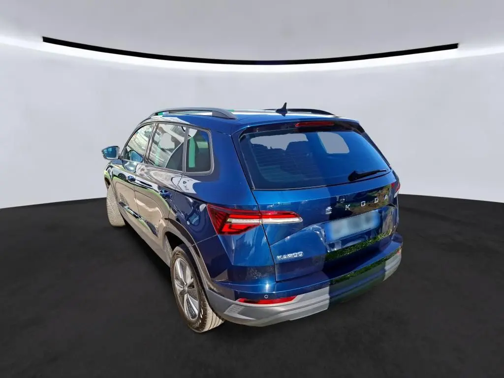 Vue 3/4 arrière droite d'un Skoda Karoq bleu métallisé avec jantes alu 17 pouces et toit avec barres de pavillon noires.