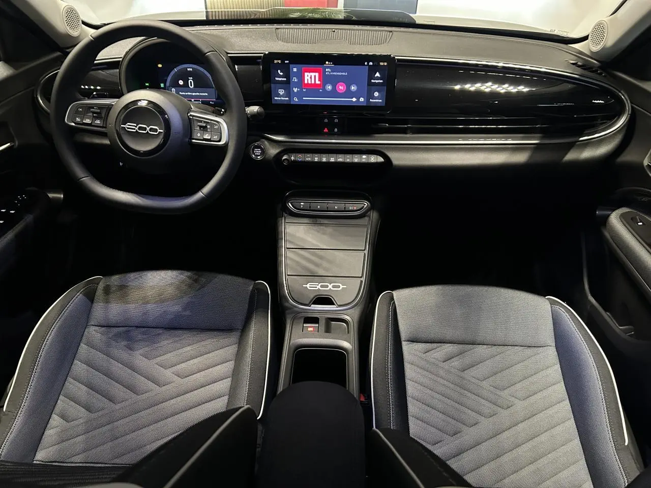 Vue intérieure avant de la Fiat 600 noire, tableau de bord avec écran tactile, volant multifonctions et sellerie bicolore jacquard.