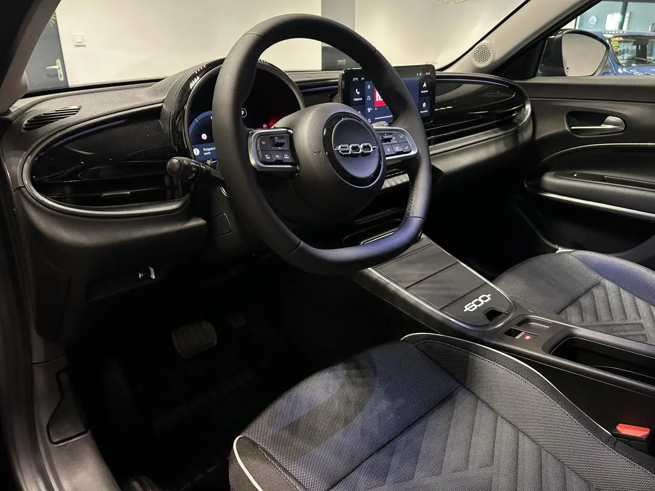 Vue intérieure côté conducteur du Fiat 600 noir, mettant en valeur le volant multifonctions et la console centrale épurée.