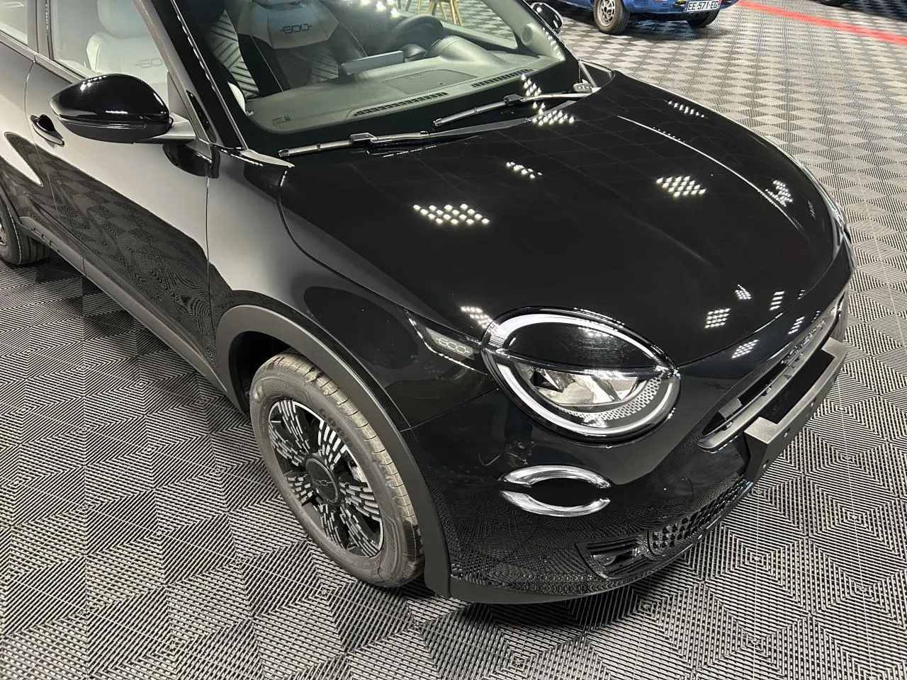 Vue 3/4 avant droit de la Fiat 600 noire avec jantes stylisées et phares ronds distinctifs en intérieur showroom.