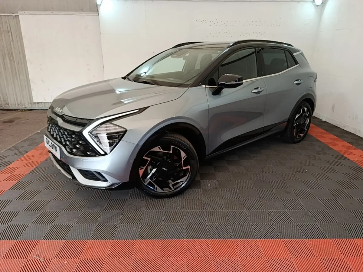 KIA Sportage gris clair en 3/4 avant droit, avec calandre noire et jantes noires à motifs géométriques.