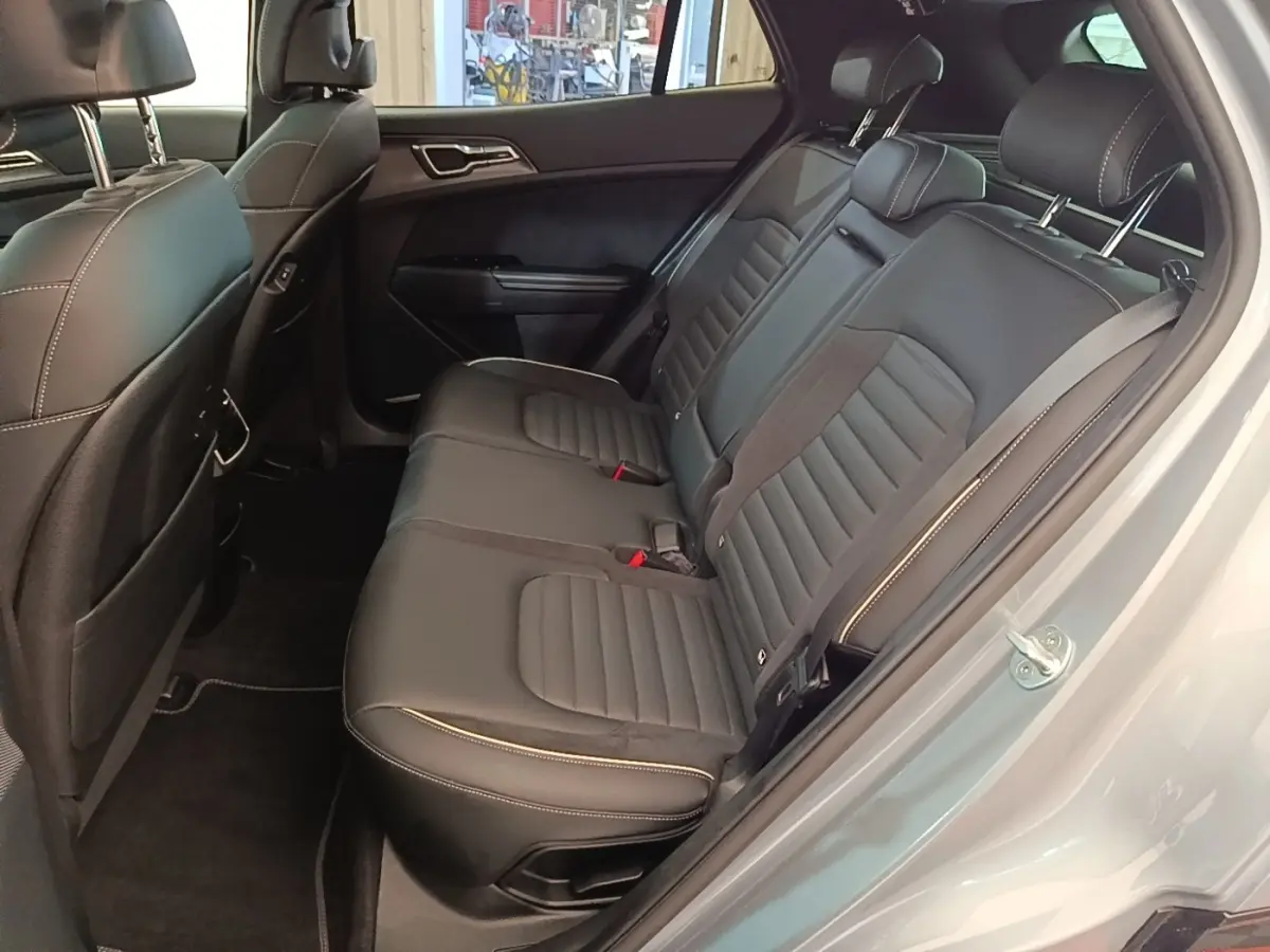 Vue intérieure côté droit montrant la banquette arrière en cuir noir avec surpiqûres blanches du Kia Sportage gris clair 2022.