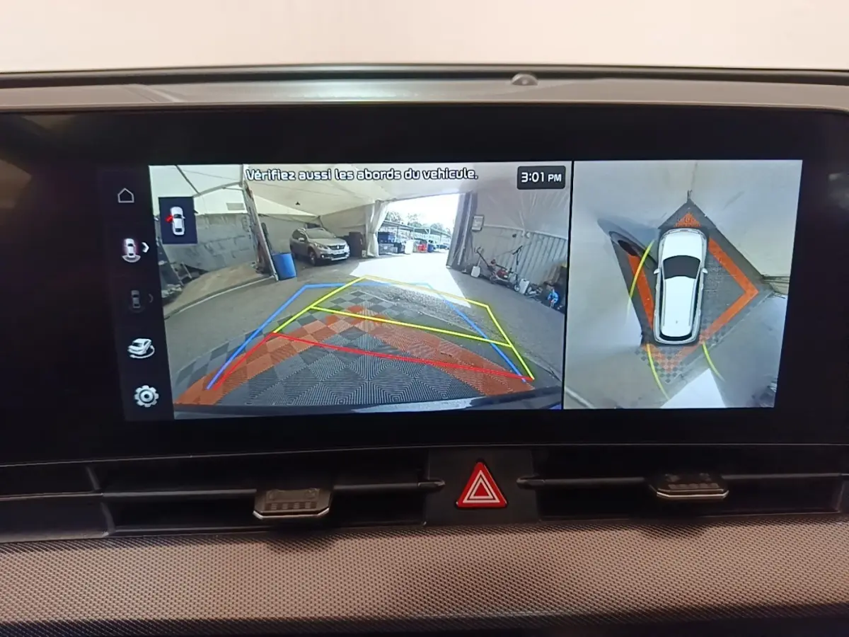 Écran tactile du tableau de bord montrant la caméra 360° et l’aide au stationnement du Kia Sportage gris clair, vue intérieure.