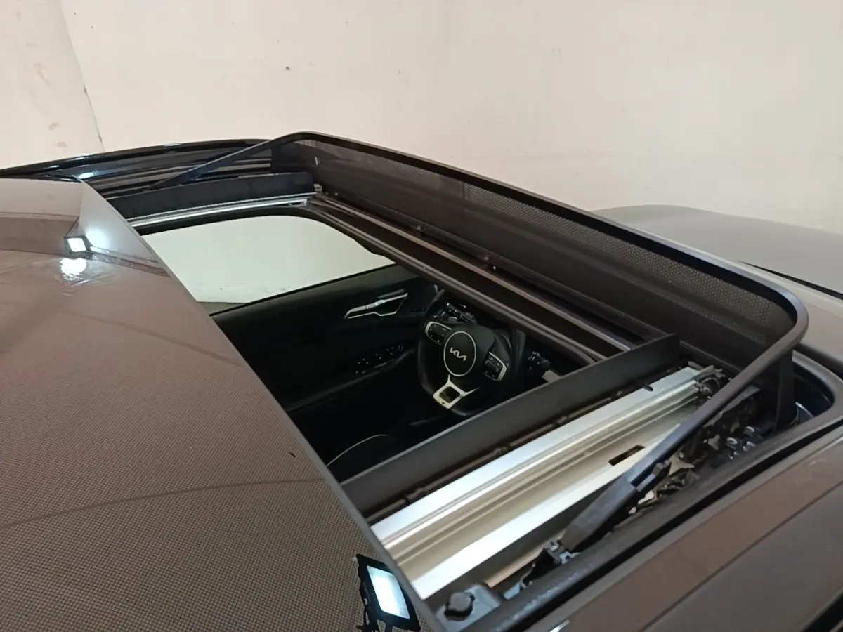 Vue plongeante sur le toit ouvrant ouvert d’un Kia Sportage gris clair, avec aperçu du volant multifonctions intérieur.