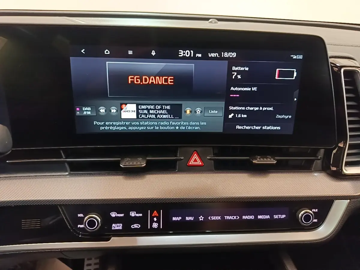 Écran tactile central du tableau de bord du Kia Sportage gris clair, affichant radio et informations batterie.