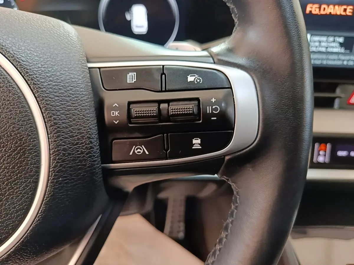 Gros plan sur les commandes du volant cuir noir du Kia Sportage hybride rechargeable, boutons multifonctions visibles.