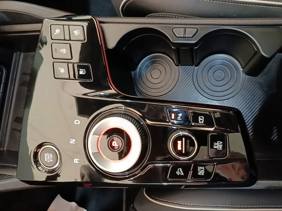 Vue rapprochée de la console centrale noire brillante du Kia Sportage hybride rechargeable avec sélecteur rotatif et boutons multifonctions.