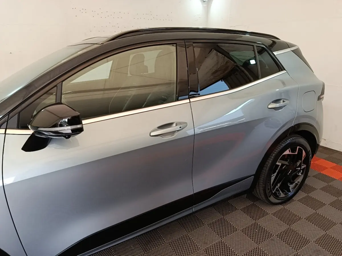 Vue de profil côté gauche d’un KIA Sportage gris clair avec toit noir et jantes noires stylisées.