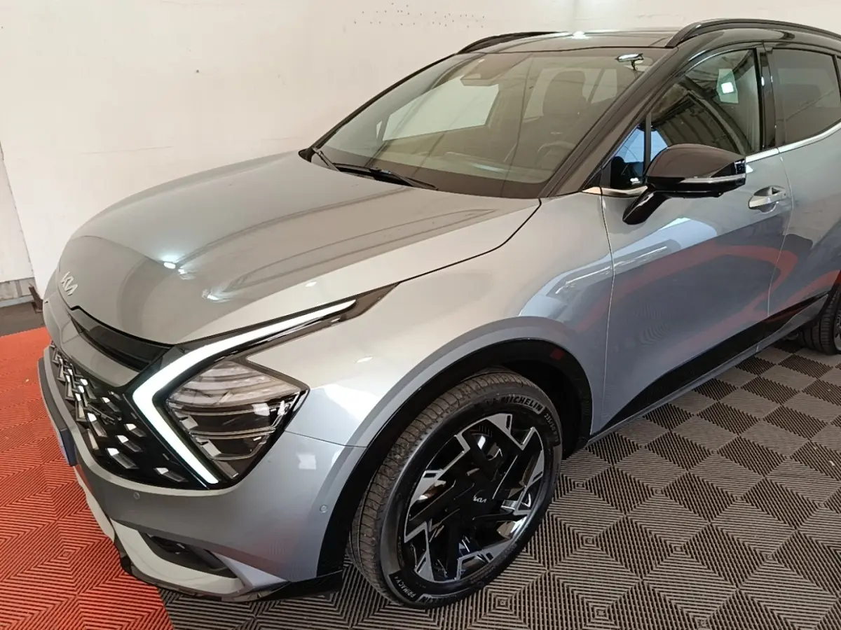 Vue 3/4 avant droit d’un KIA Sportage gris clair avec feux LED en forme de C et jantes noires distinctives.