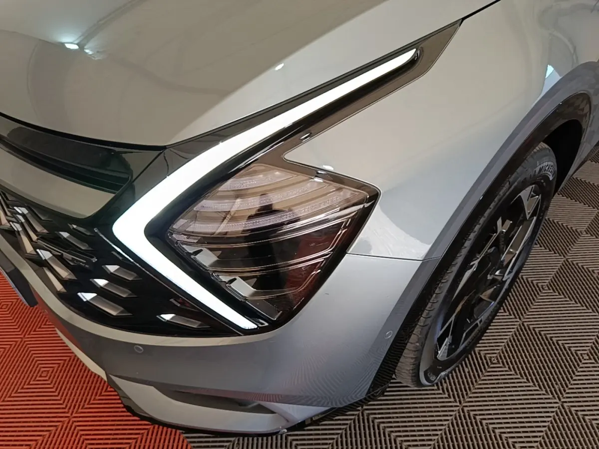 Gros plan sur l'avant droit gris clair du Kia Sportage 2022, mettant en valeur son phare LED en forme de boomerang.