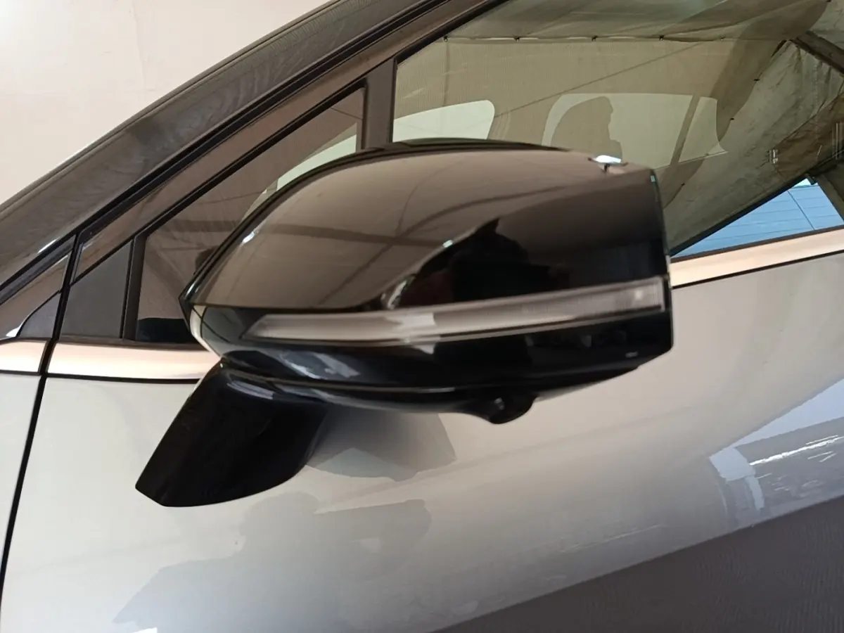 Rétroviseur noir brillant côté gauche du Kia Sportage gris clair, avec fenêtre et partie de la porte visibles.