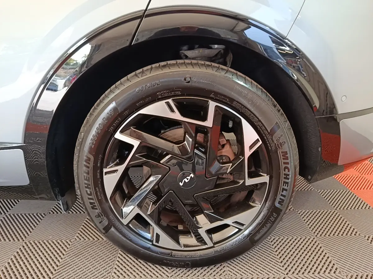 Gros plan sur la roue arrière droite d’un KIA Sportage gris clair avec jante noire et argentée au design géométrique.