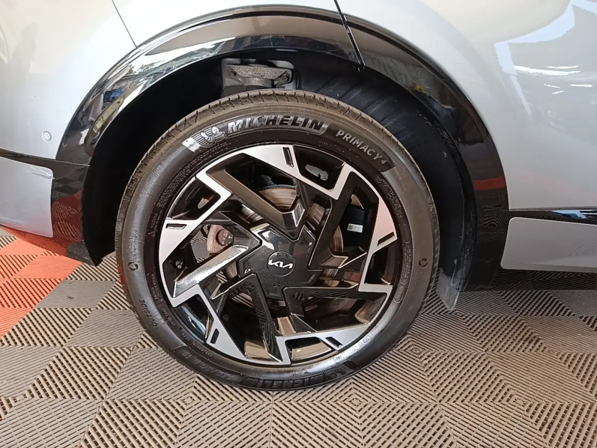 Gros plan sur la roue avant droite d’un KIA Sportage gris clair avec jante noire et argentée au design géométrique.