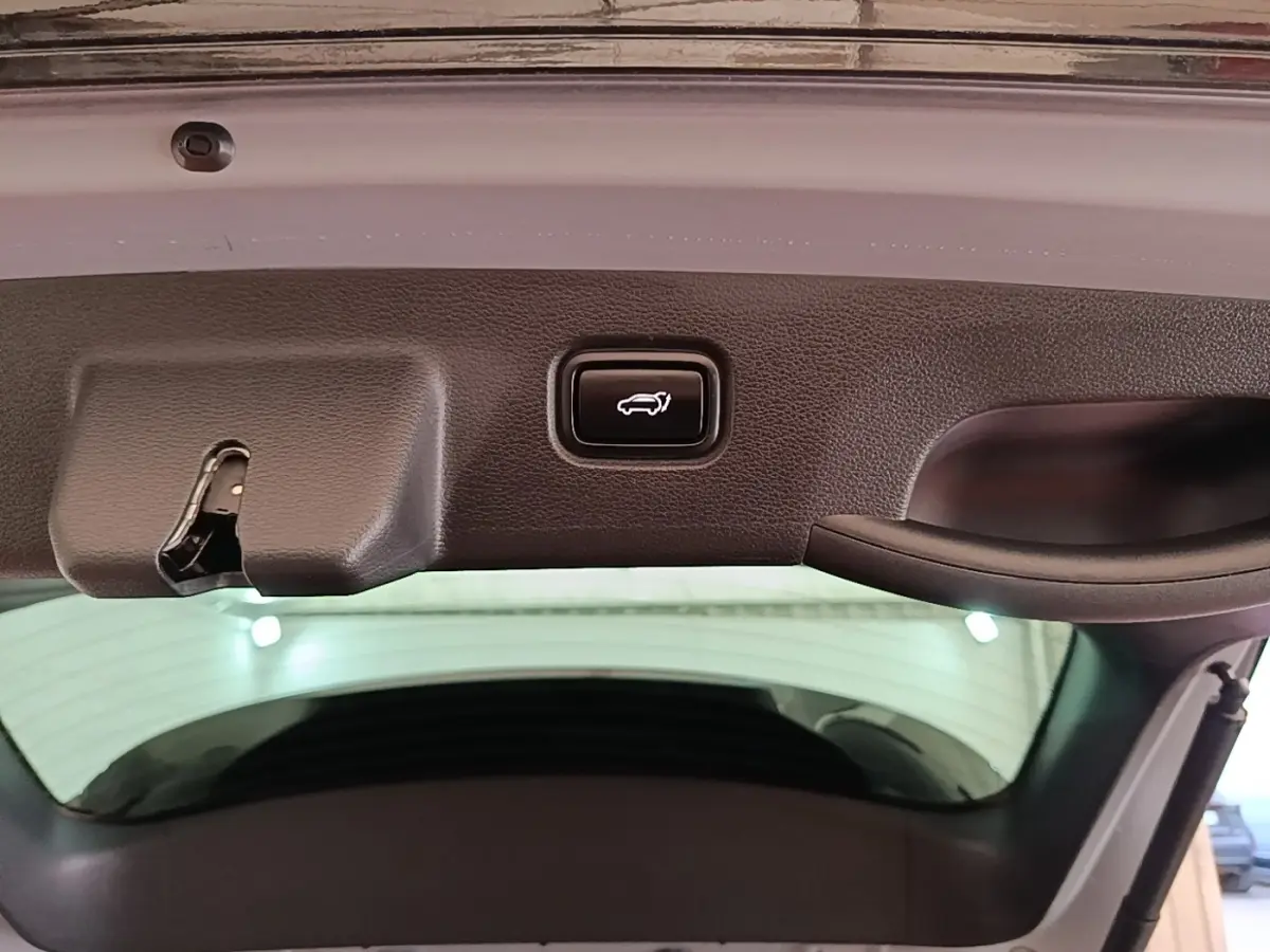 Bouton d'ouverture électrique du coffre sur la partie intérieure du hayon d'un KIA Sportage gris clair, vue rapprochée.
