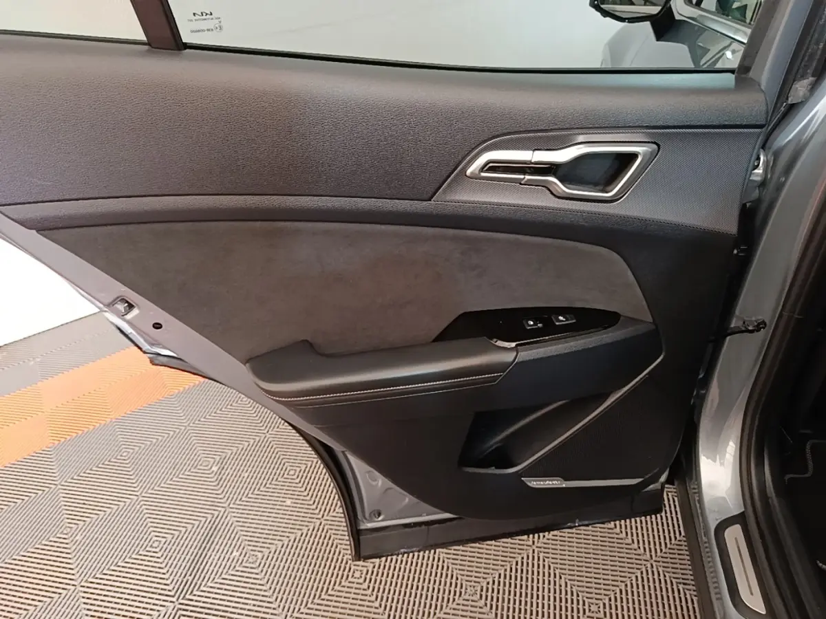 Vue intérieure de la porte arrière gauche gris clair du KIA Sportage 2022 avec garniture noire et commandes de fenêtre.
