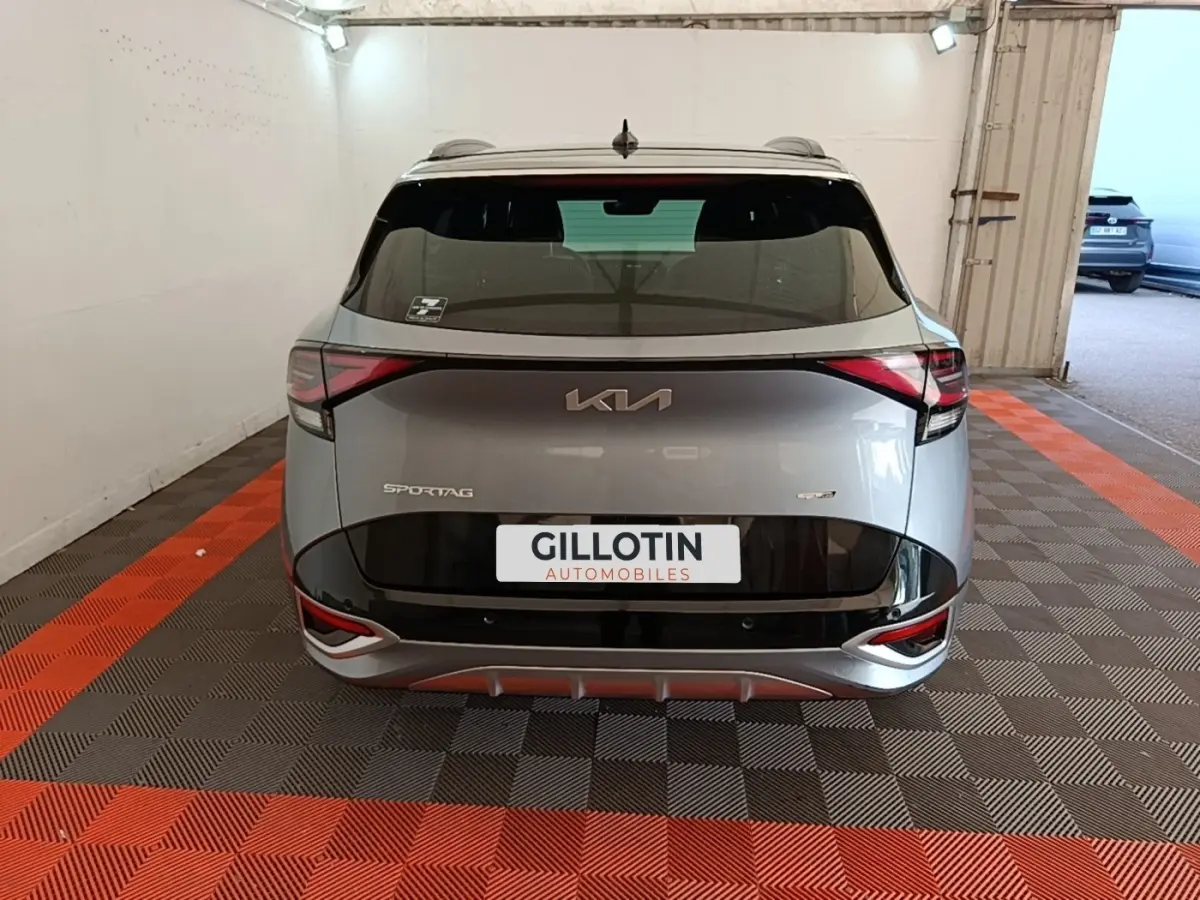 Vue arrière d'un KIA Sportage gris clair 2022 avec logo moderne et feux arrière en forme de flèche dans un garage.