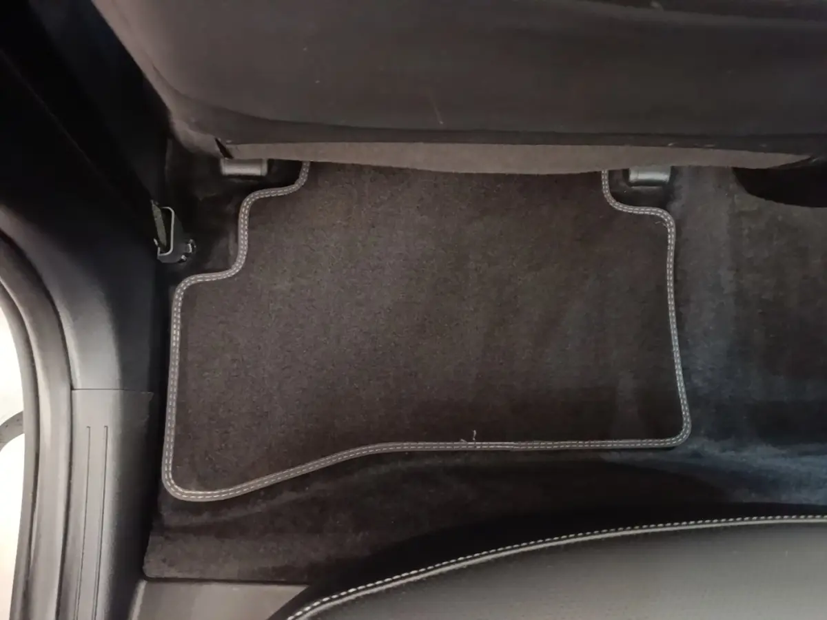 Détail du tapis de sol arrière noir avec surpiqûres blanches dans un KIA Sportage gris clair 2022.