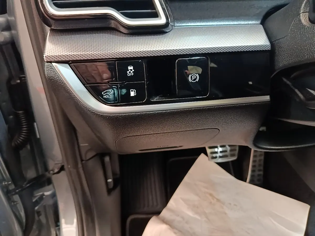 Détail des commandes côté gauche sous le tableau de bord du Kia Sportage gris clair 2022, avec boutons de frein à main et assistance.