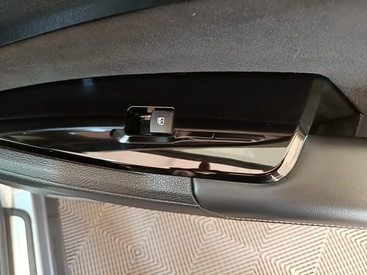 Détail du bouton de commande de lève-vitre sur la porte intérieure d’un Kia Sportage gris clair.