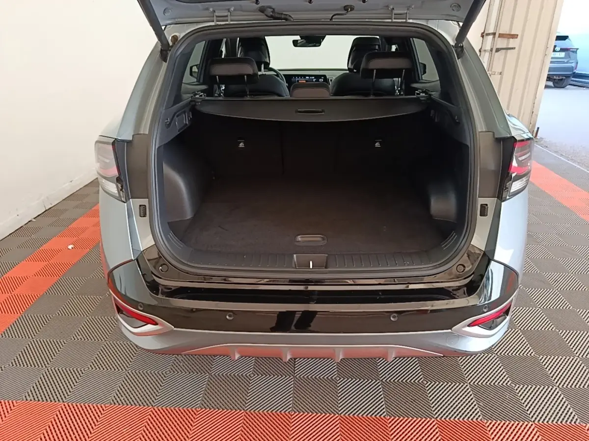 Vue arrière ouverte du coffre d’un KIA Sportage gris clair 2022, avec seuil de chargement noir brillant et intérieur spacieux.