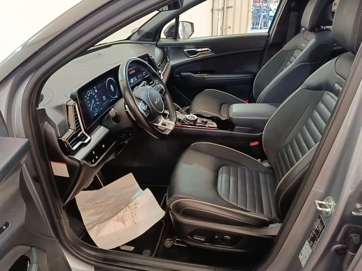 Vue intérieure côté conducteur du Kia Sportage gris clair 2022, avec tableau de bord digital et sièges en cuir noirs GT-Line.