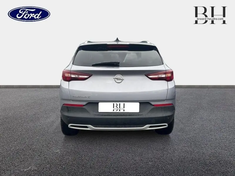 Vue arrière d'un Opel Grandland X gris quartz avec toit et rétroviseurs noirs, en extérieur sur sol goudronné.
