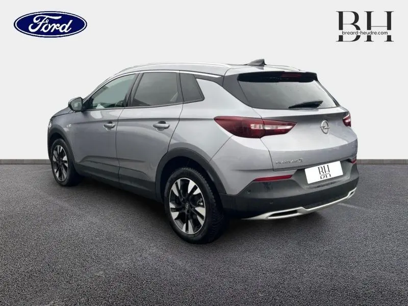 Opel Grandland X gris Quartz avec toit et rétroviseurs noirs, vue 3/4 arrière côté gauche sur fond neutre.