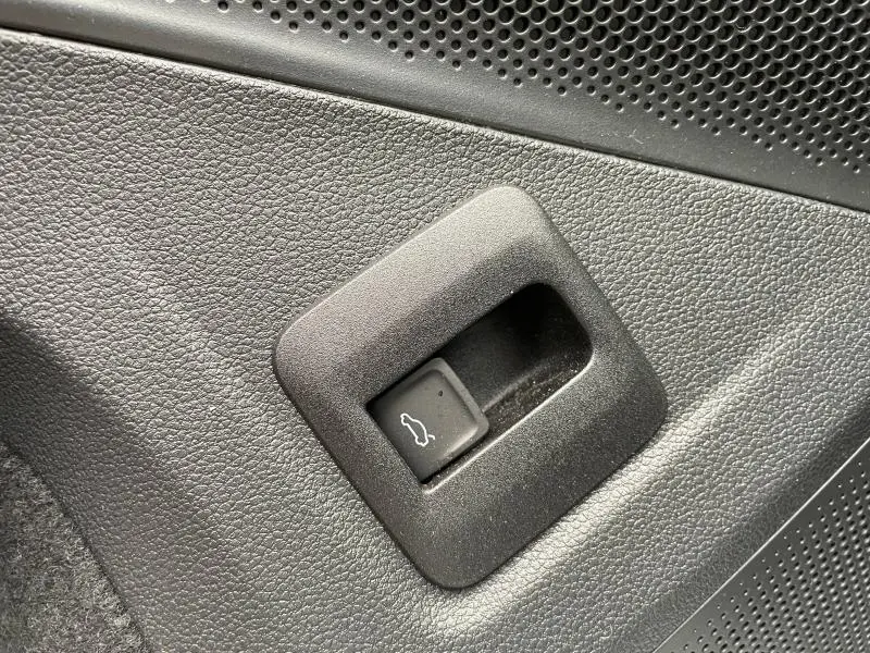 Gros plan sur le bouton d'ouverture du coffre dans l'habitacle noir du Volkswagen Tiguan blanc 2025.