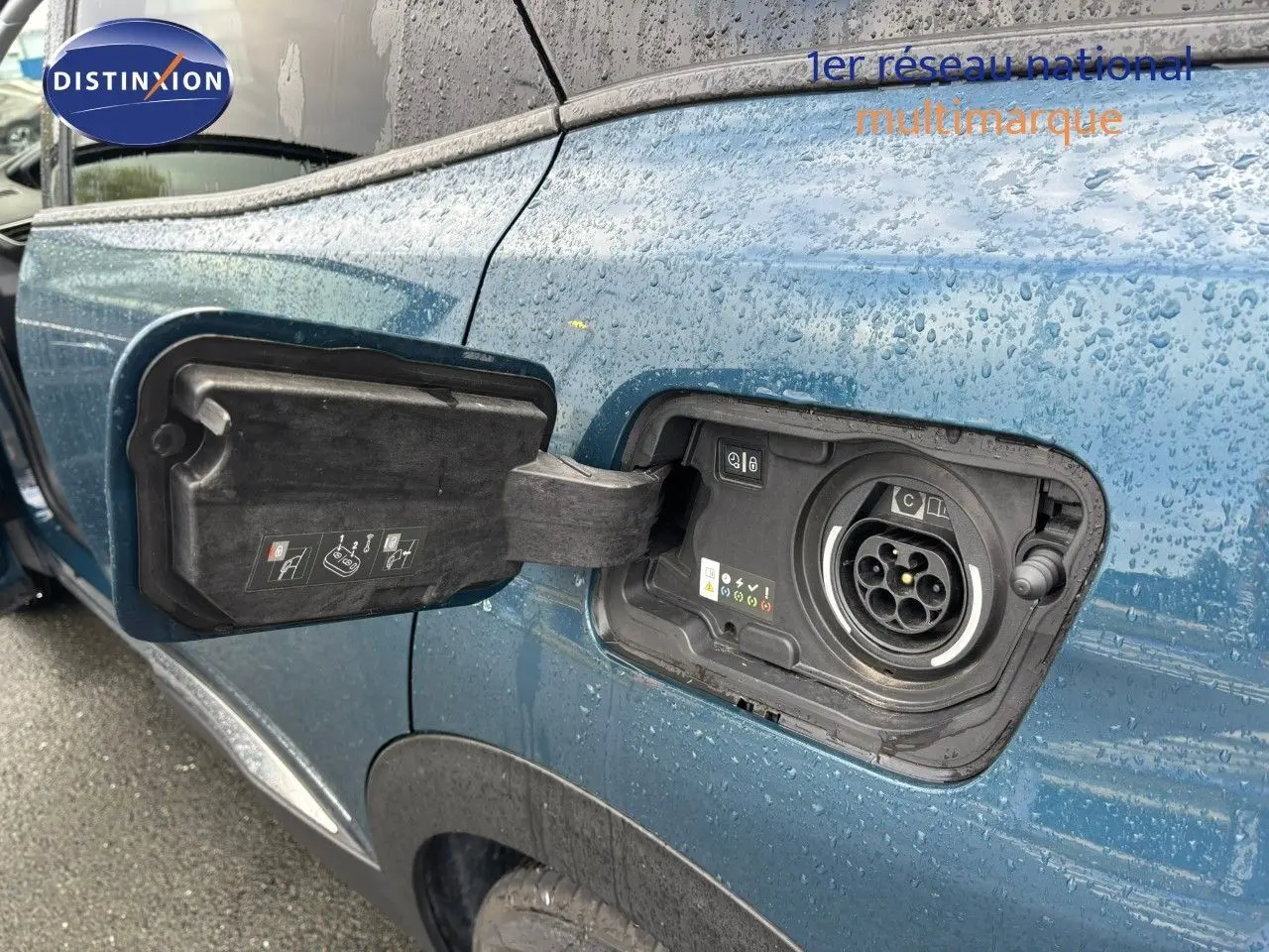 Détail de la trappe de recharge ouverte côté gauche sur Peugeot 3008 hybride rechargeable bleu Celebes métal sous la pluie.