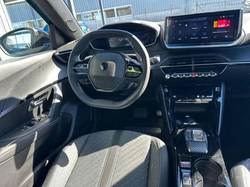 Vue intérieure de face du poste de conduite du Peugeot 2008 Hybrid 2025 avec volant compact, écran tactile et finitions noires modernes.