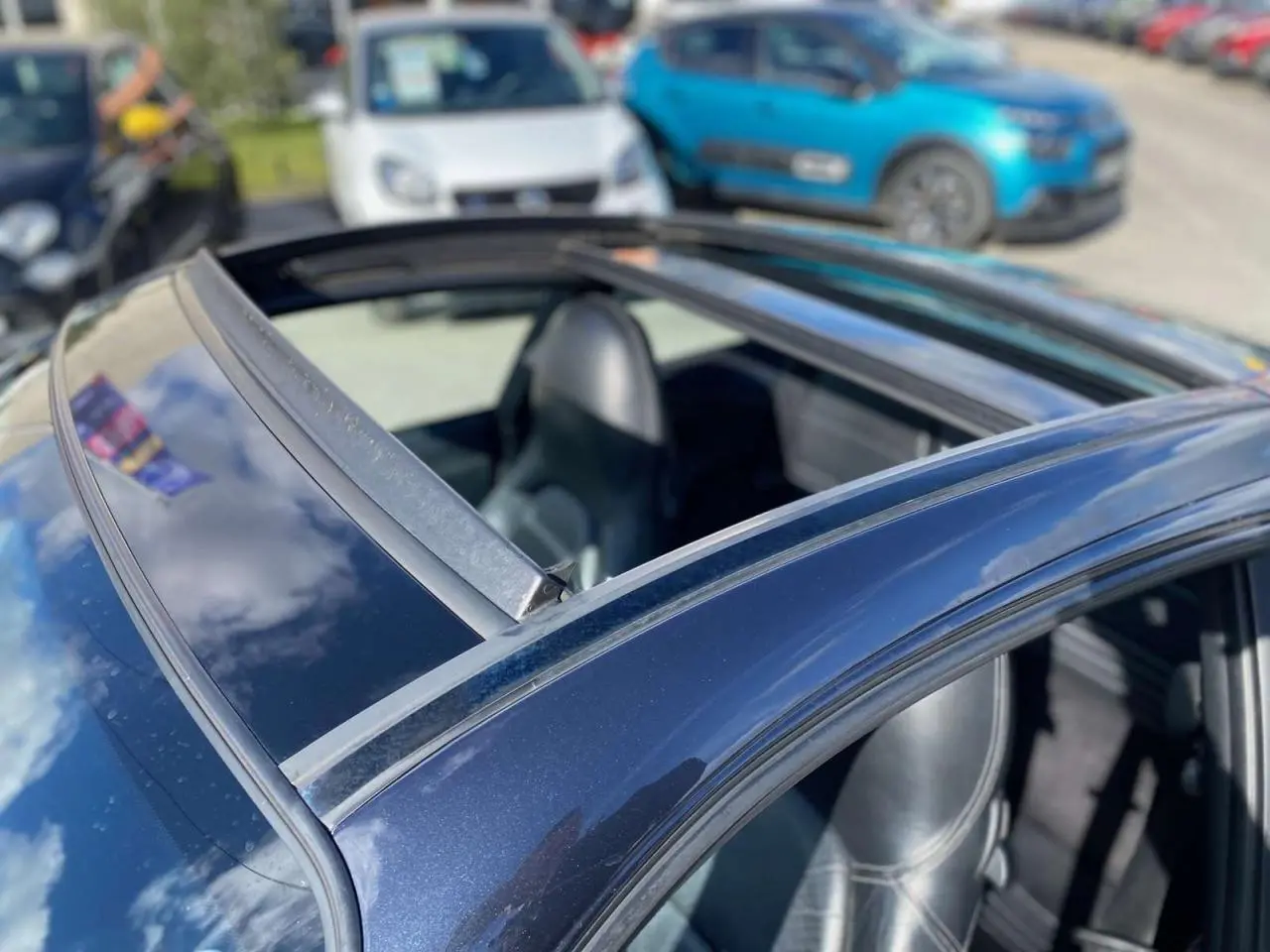 Vue rapprochée du toit coulissant ouvert d’une Porsche 911 Targa gris foncé, avec sellerie cuir noire visible.