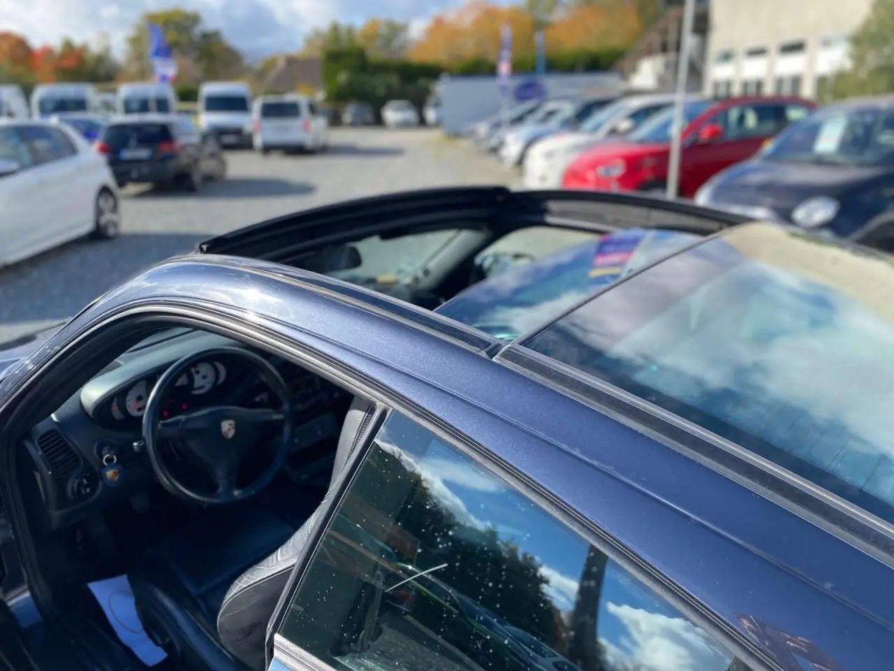 Vue côté gauche arrière d'une Porsche 911 Targa gris foncé avec toit coulissant ouvert et intérieur cuir noir visible.