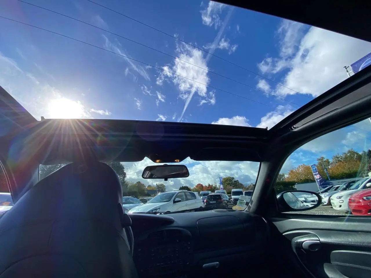 Vue intérieure avant de la Porsche 911 Targa gris foncé, toit ouvert laissant voir le ciel et le pare-brise.