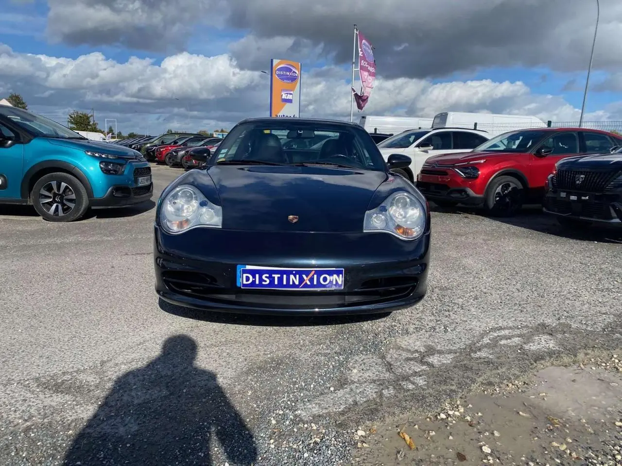 Vue avant d'une Porsche 911 Targa 996 gris foncé stationnée sur un parking sous un ciel nuageux.