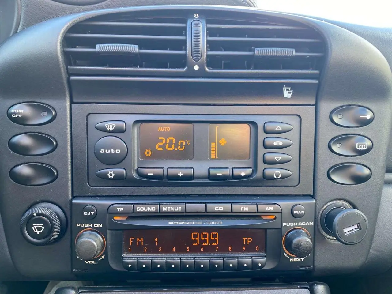 Vue rapprochée du tableau de bord noir de la Porsche 911 Targa 996 gris foncé, montrant la climatisation et la radio d'origine.