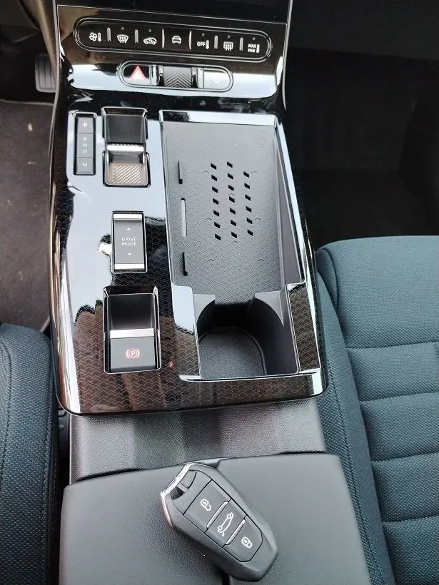 Vue rapprochée de la console centrale noire brillante du Citroën C5 Aircross 2026 avec clé posée sur l'accoudoir tissu bleu.