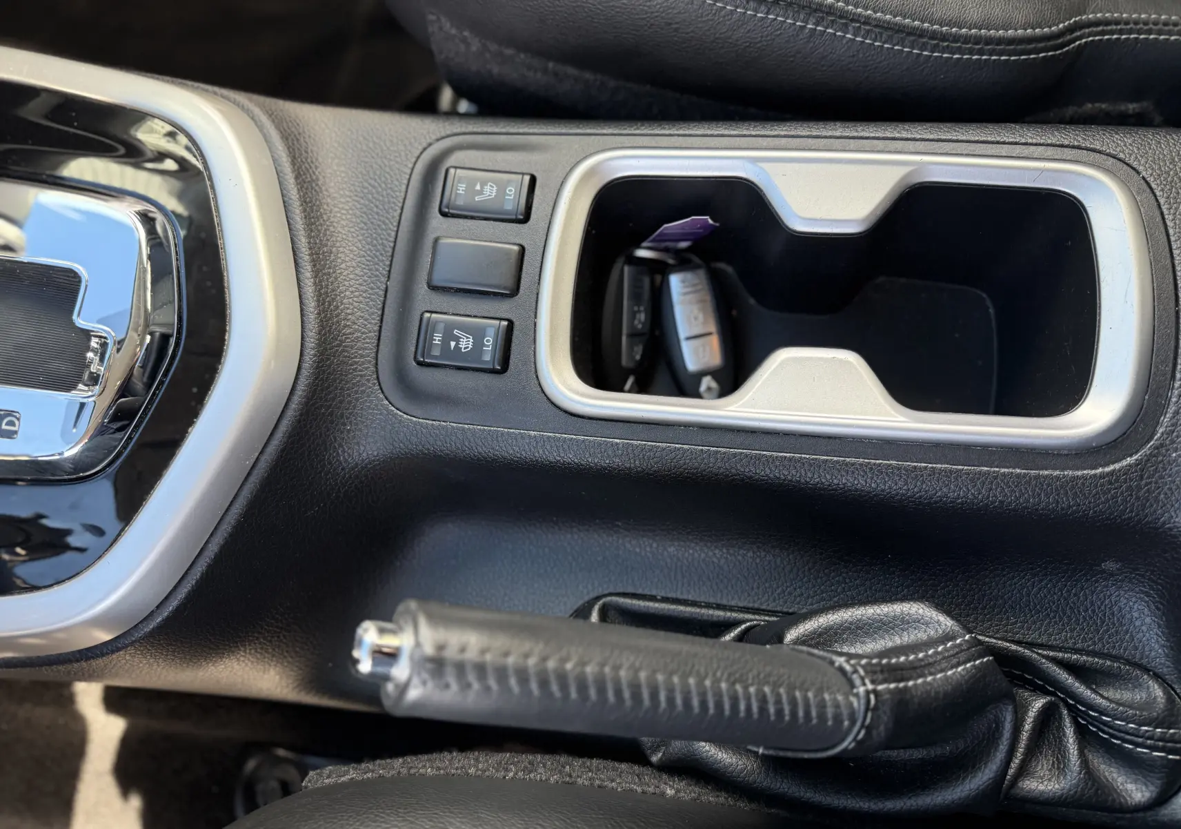 Vue rapprochée de la console centrale en cuir noir du Renault Alaskan 2018 avec levier de frein à main et commandes de sièges chauffants.